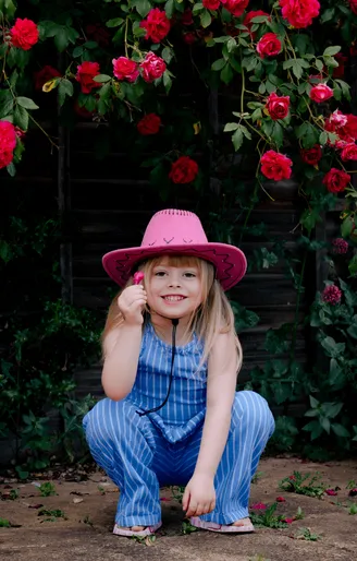Young girl in a pink cowboy hat among roses